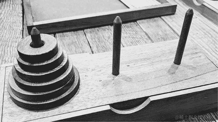 图片上是一个木制表面，上面有三根杆，第一根杆上放着一堆圆盘，从底部到顶部尺寸逐渐减小。