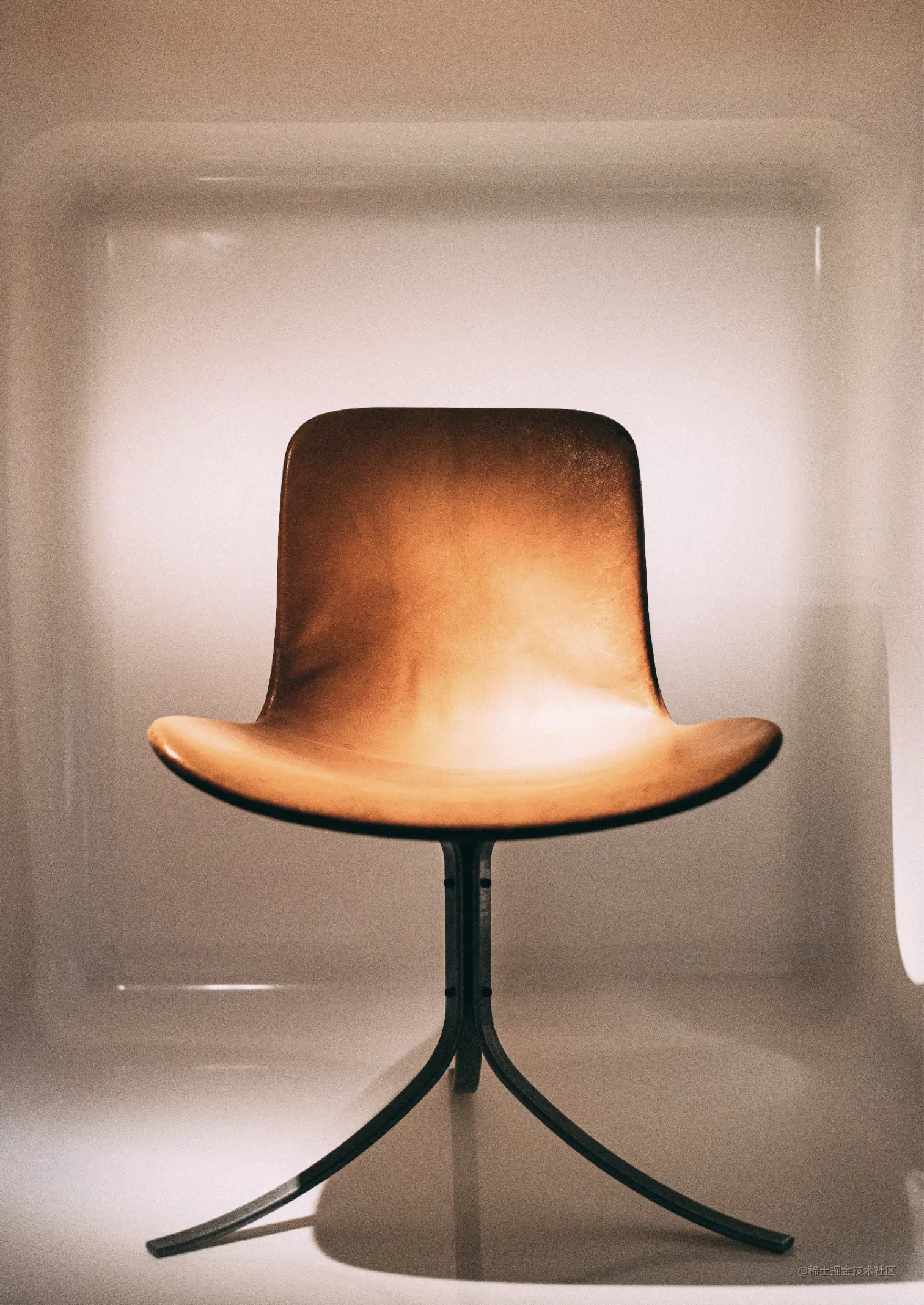 A brown leather black chair with a seamless back facing directly at the camera, with three curved black legs.